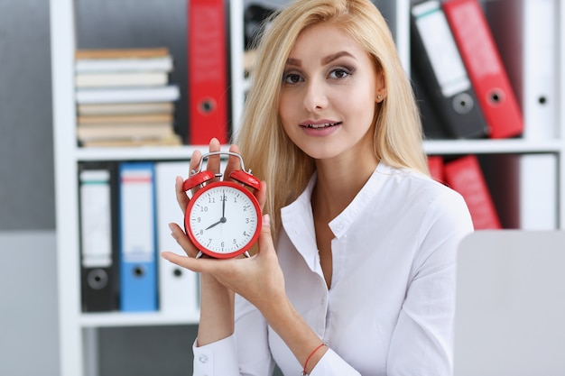 Sonriente mujer de negocios sosteniendo en la mano en el despertador un color rojo que muestra las ocho de la mañana o la tarde AM PM