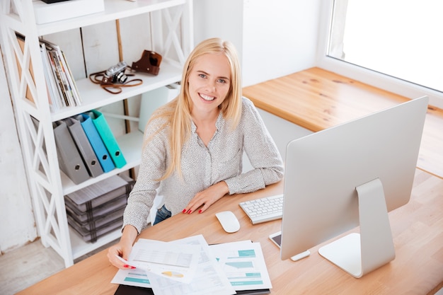 Sonriente mujer de negocios trabajando con papeles y computadora en Office