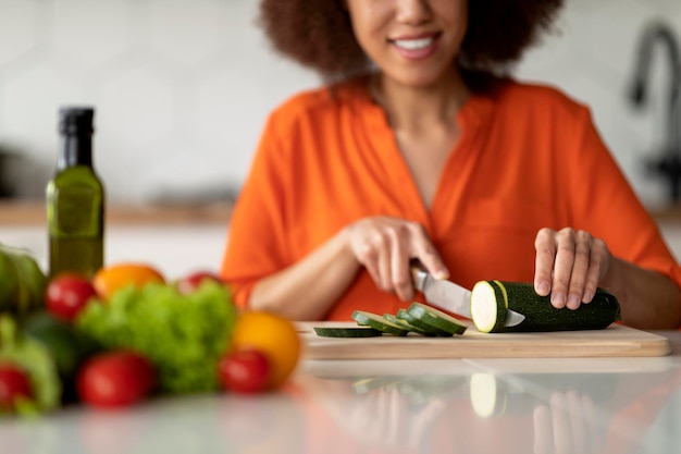 Sonriente mujer negra picar calabacín calabacín mientras cocina comida en la cocina