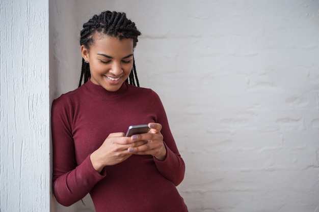 Sonriente mujer negra Texting en Smartphone por la pared