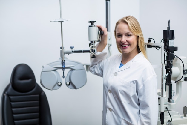 Sonriente mujer optometrista de pie cerca de foróptero