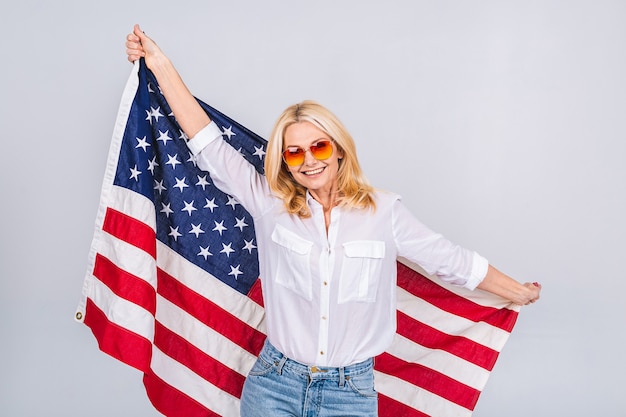 Sonriente mujer patriótica hermosa senior vistiendo la bandera de Estados Unidos aislado sobre fondo blanco con una cara de sorpresa.