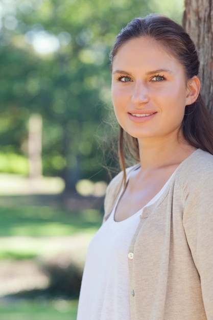 Sonriente mujer de pie junto a un árbol