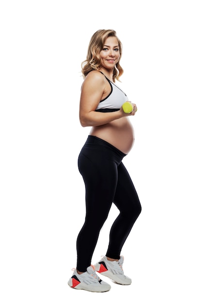 Sonriente mujer rubia embarazada en ropa deportiva con pesas