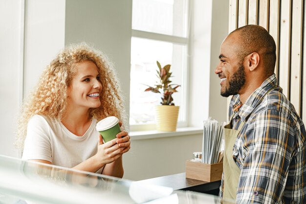 Sonriente mujer rubia hablando con un camarero de una cafetería.