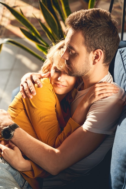 Sonriente mujer rubia joven y bonita y un hombre caucásico sereno dormitando pacíficamente en el sofá