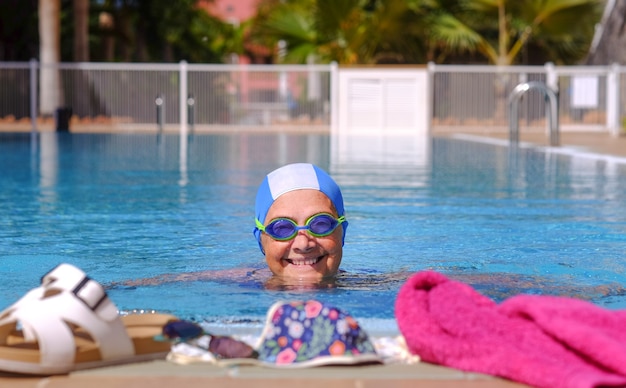 Sonriente mujer senior swimm en la piscina con gafas de natación y gorra - jubilado activo disfrutando de un estilo de vida saludable