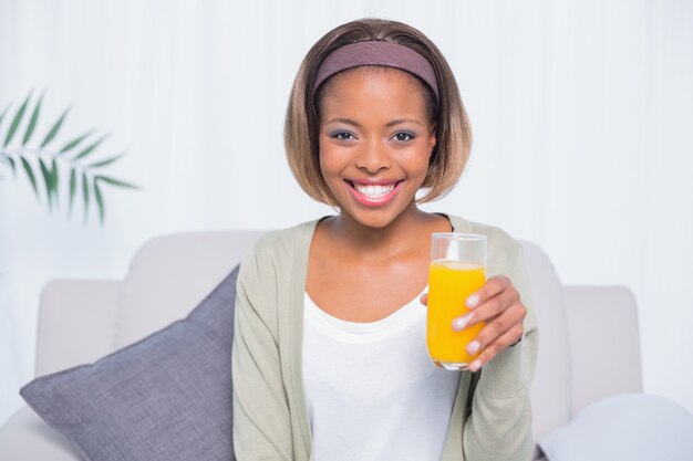 Sonriente mujer sentada en el sofá con vaso de jugo de naranja