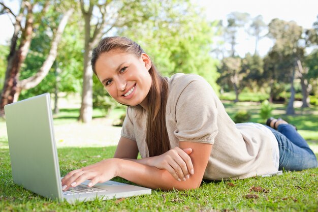 Sonriente mujer tendida en el césped con su computadora portátil