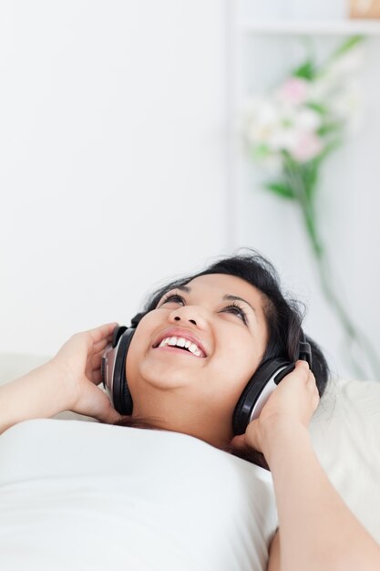 Sonriente mujer tendida en un sofá con auriculares en