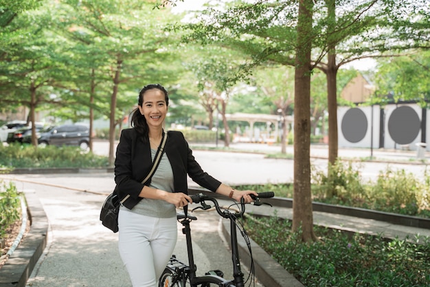 Sonriente mujer trabajadora camina en su bicicleta plegable por el parque