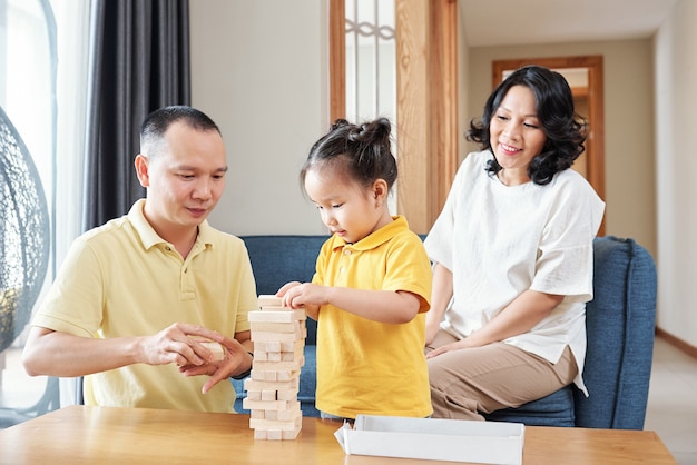 Sonriente mujer vietnamita mirando a su marido y su pequeña hija haciendo torre de pequeños palos de madera