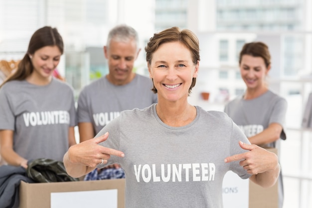 Sonriente mujer voluntaria señalando en la camisa