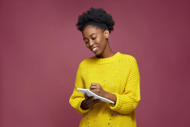 Sonriente niña afroamericana creativa escribiendo ideas programar metas sueños en la planificación del bloc de notas