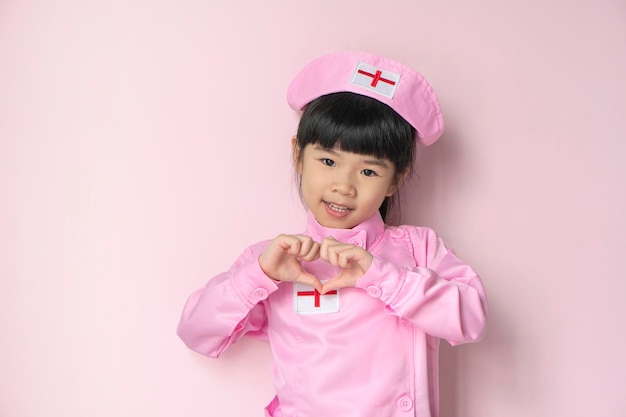 Sonriente niña asiática en uniforme médico Salud y concepto médico aislado sobre fondo rosa