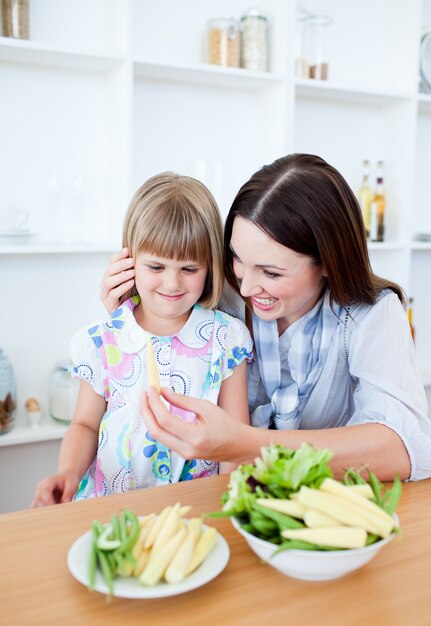 Sonriente niña comiendo verduras con su madre