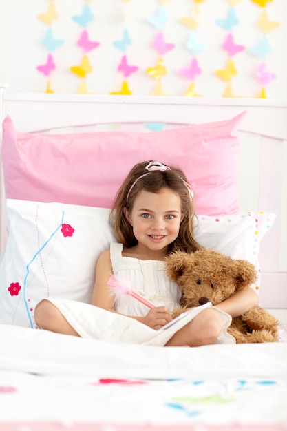 Sonriente niña escribiendo en la cama