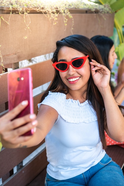 Sonriente niña latina tomando una foto con su teléfono para sus redes sociales.