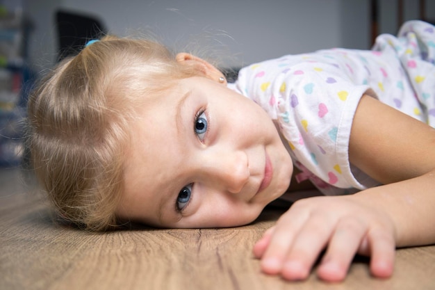 Sonriente niña linda niña en camiseta acostada en el piso de madera