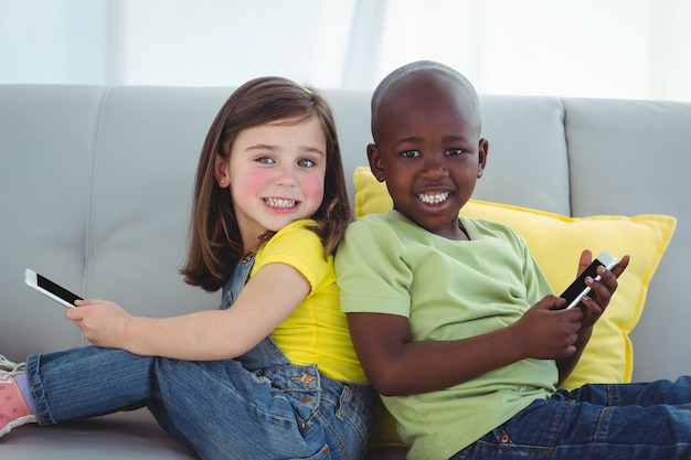 Sonriente niña y niño usando teléfonos móviles