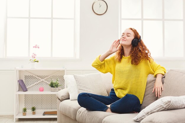 Sonriente niña pelirroja escuchando música en línea en teléfonos inteligentes en auriculares.