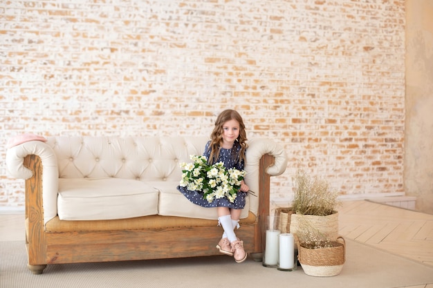 Sonriente niña de pelo rizado con un ramo de flores de jazmín se sienta en el sofá