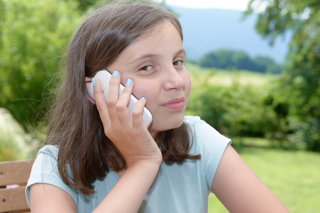 Sonriente niña pre adolescente llamando en teléfono inteligente, al aire libre