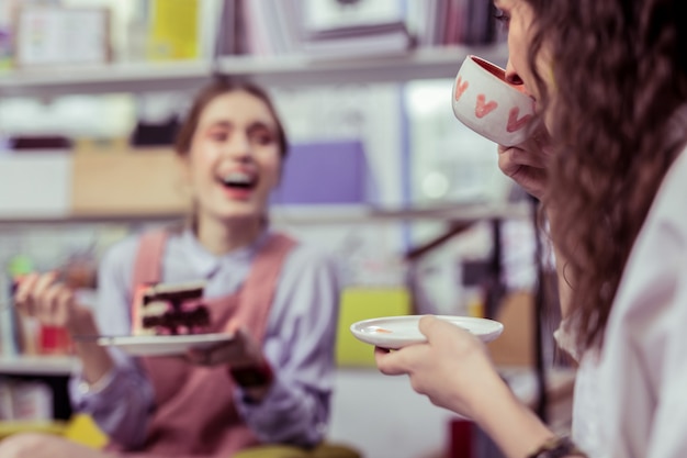 Foto sonriente niña radiante. riendo alegres señoras bebiendo té y comiendo postre durante un tiempo de paz con un amigo cercano