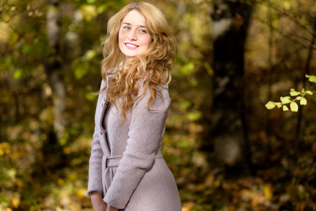 Sonriente niña rubia en ropa fría en el bosque