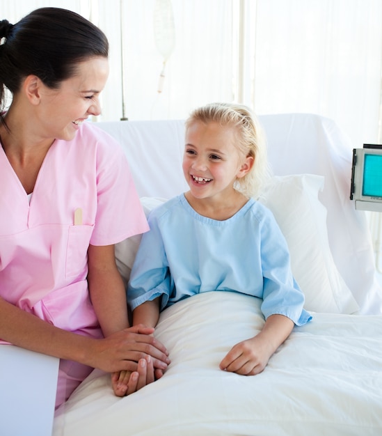 Sonriente niña sentada en una cama de hospital con su médico