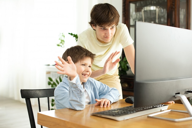 Sonriente niño y adolescente chateando en línea y mirando la pantalla de la computadora