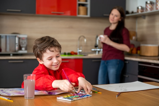 Sonriente niño dibujando en la cocina con mamá