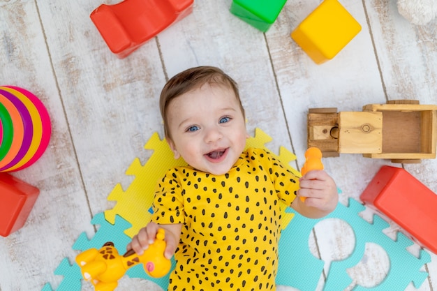 Sonriente niño feliz juega en la guardería con un traje amarillo con juguetes de colores brillantes