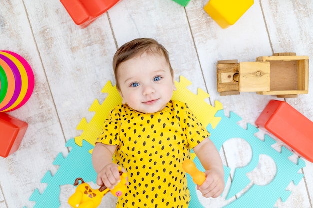 Sonriente niño feliz juega en la guardería con un traje amarillo con juguetes de colores brillantes