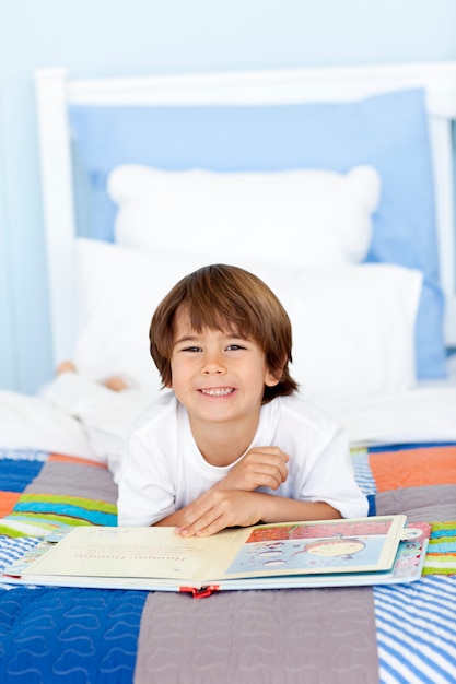 Sonriente niño leyendo en la cama