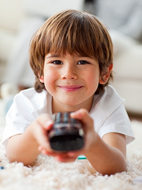 Sonriente niño mirando televisión acostado en el piso