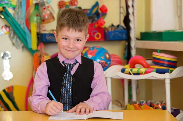 Sonriente niño preescolar en su escritorio Niño de seis años con bolígrafo y cuaderno