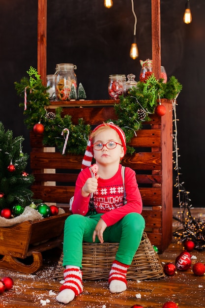 Sonriente niño rubio agradable sentado en el piso de madera con bolas de navidad