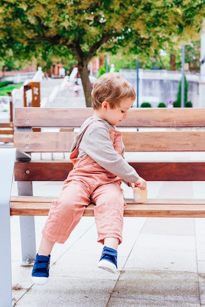 Sonriente niño de tres años agarrando el lado de una bañera sentado en un banco en la calle