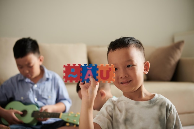 Sonriente niño vietnamita jugando con rompecabezas del alfabeto en casa