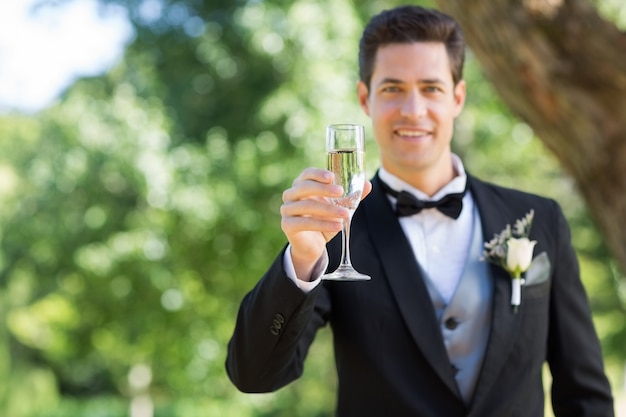 Sonriente novio con flauta de champán en el jardín