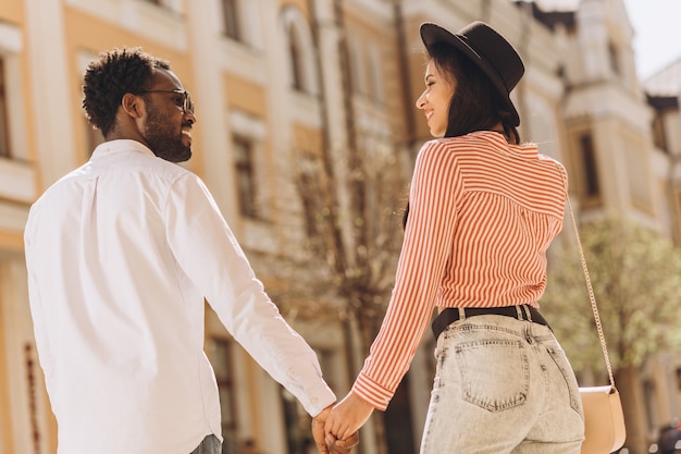 Sonriente novio y novia tomados de la mano mientras camina en la calle