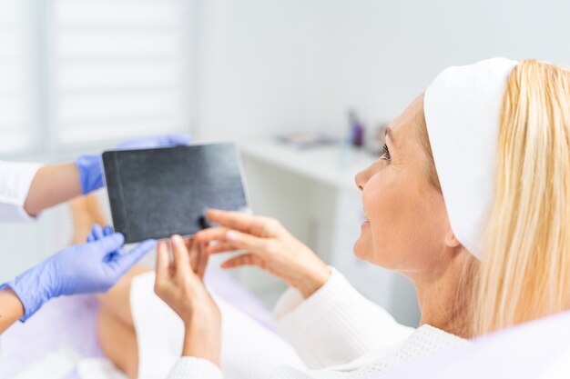 Sonriente paciente mujer rubia caucásica de mediana edad apuntando a una tableta digital en manos de su médico