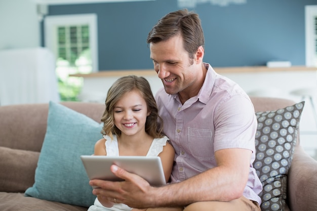 Sonriente padre e hija sentada en el sofá con tableta digital en la sala de estar