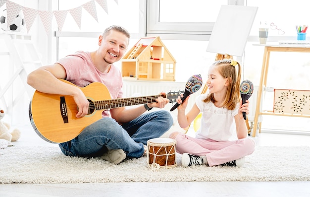 Sonriente padre e hija tocando instrumentos musicales en la habitación de los niños