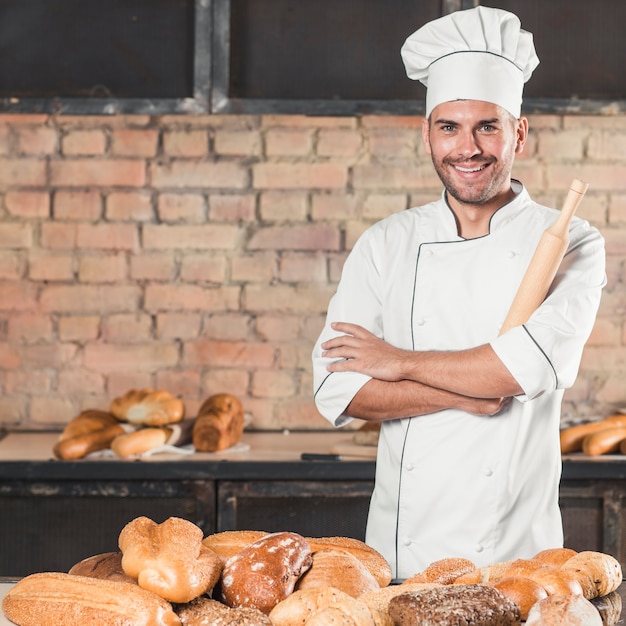 Foto sonriente panadero masculino con diferentes tipos de panes horneados en panadería