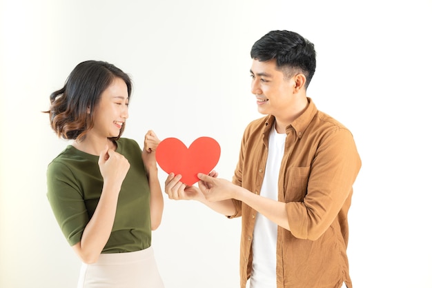 Sonriente pareja amorosa sosteniendo en forma de corazón sobre la pared blanca.