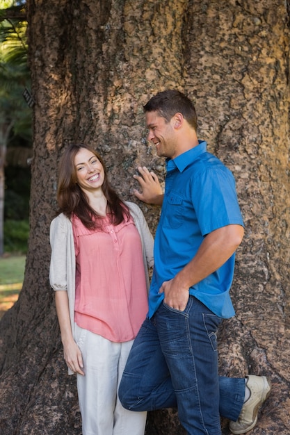 Sonriente pareja apoyándose en un árbol