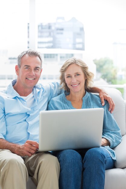 Foto sonriente pareja descansando en su sofá usando la computadora portátil