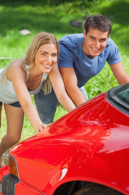 Sonriente pareja empujando su coche averiado